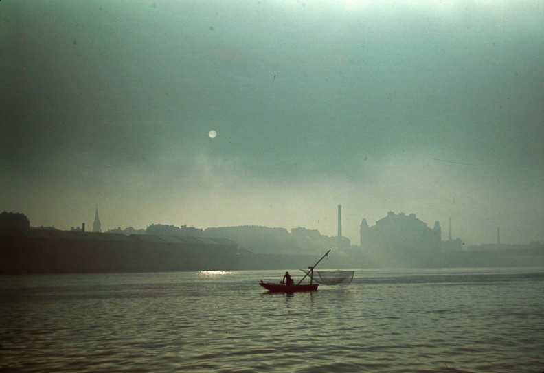 halász a Dunán, háttérben a Közraktárak és az Elevátor-ház.